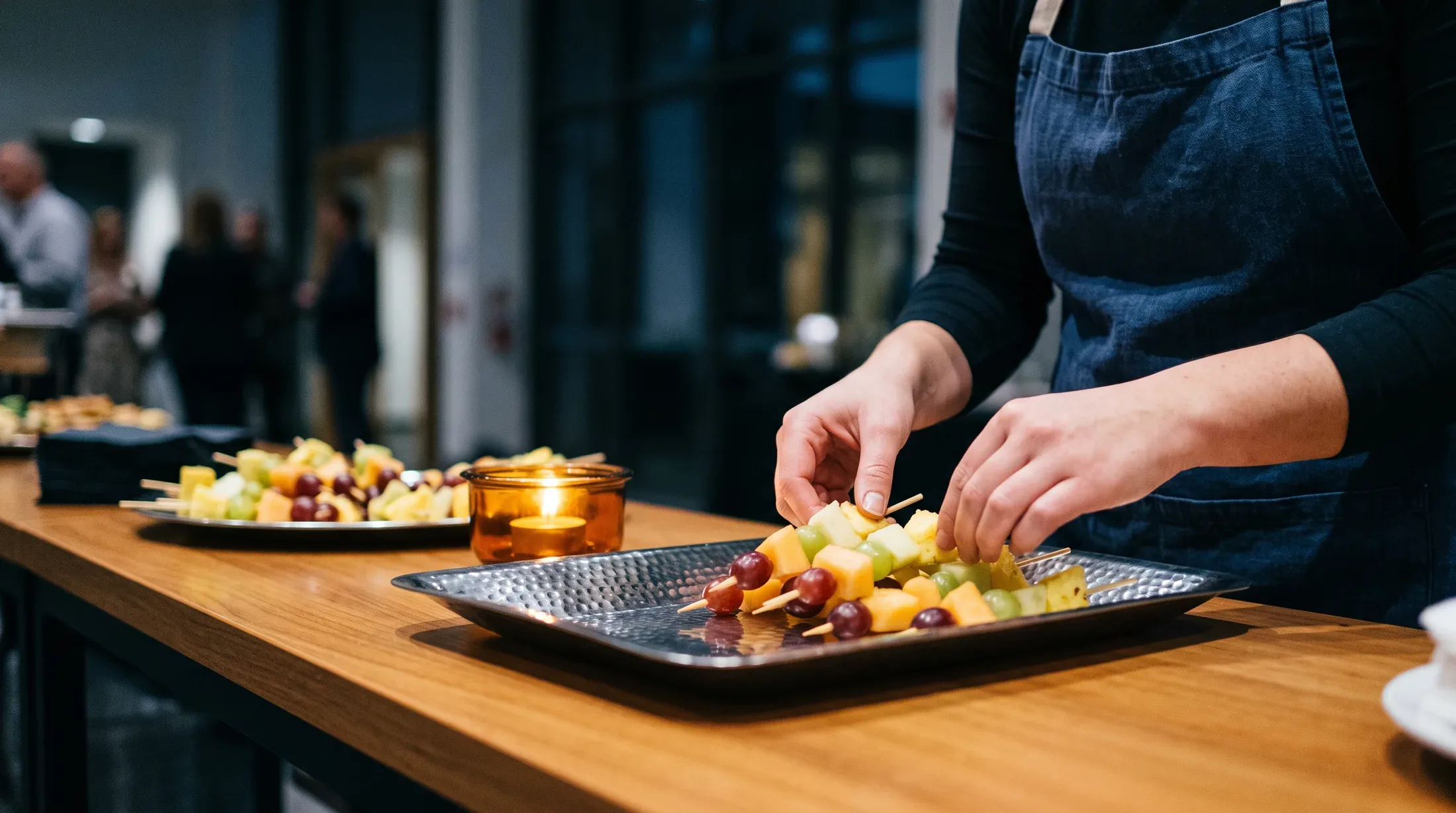 A catering crew member's hands arranging fruit skewers on a buffet tray