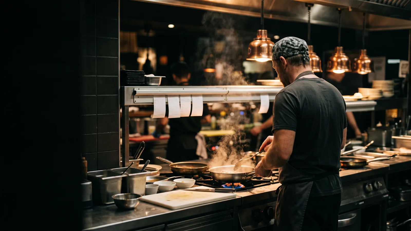 A line cook working a saute pan at the pass under heat lamps