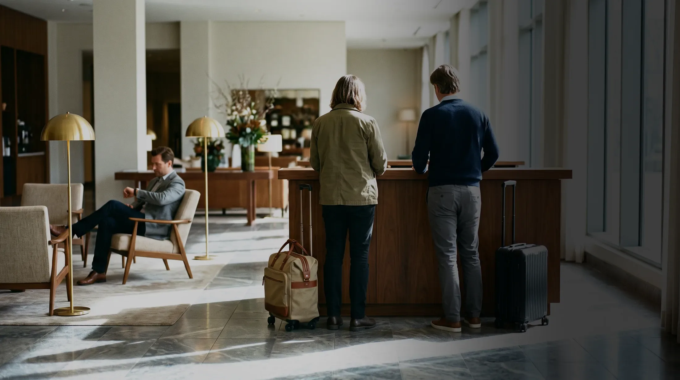 Two guests waiting with luggage at a reception desk with nobody behind it