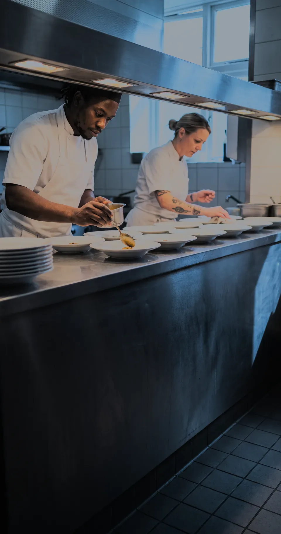 Two chefs plating a row of dishes down a pass