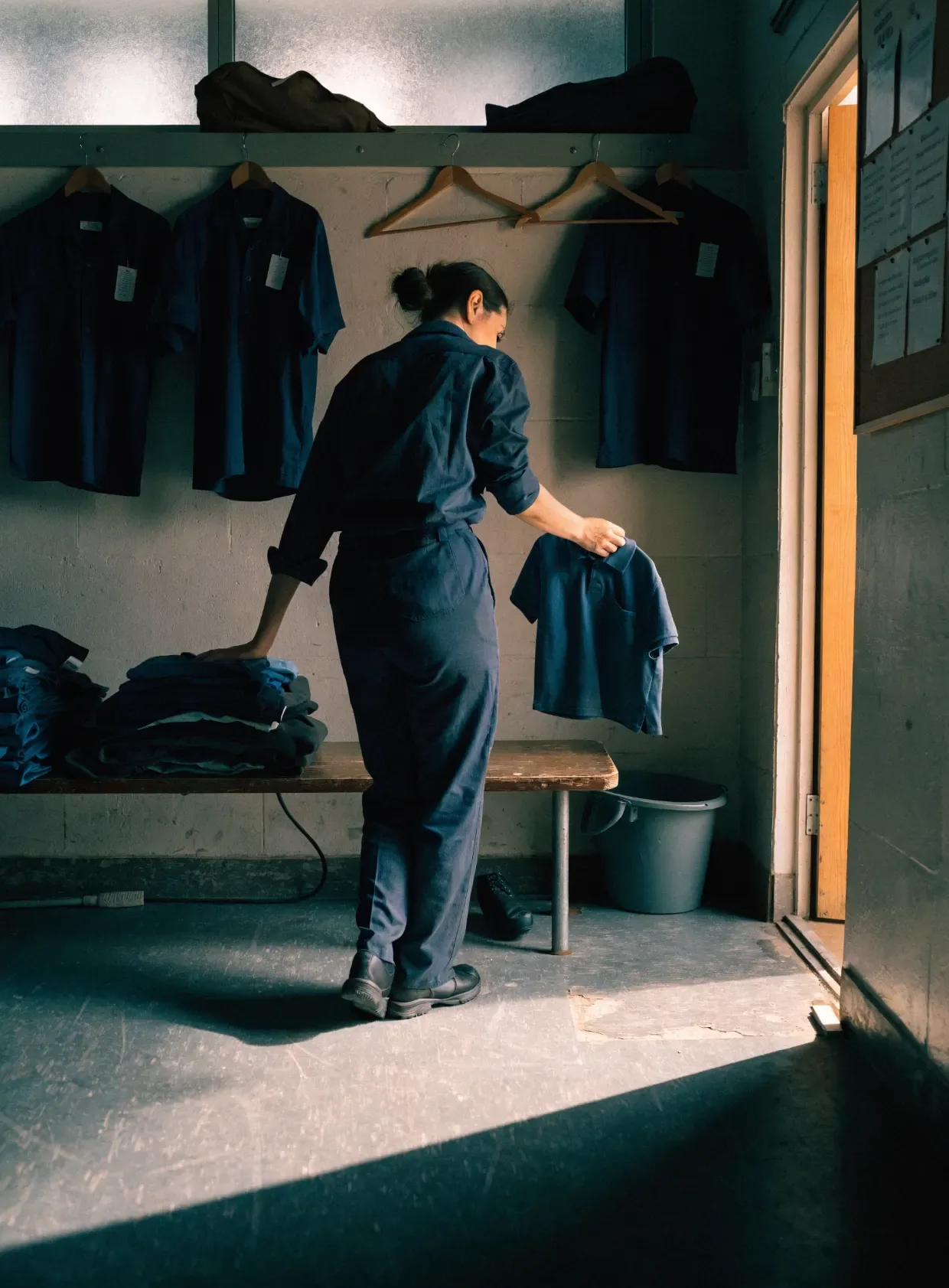 A worker lifting a clean uniform off the rail in a crew room before a shift.