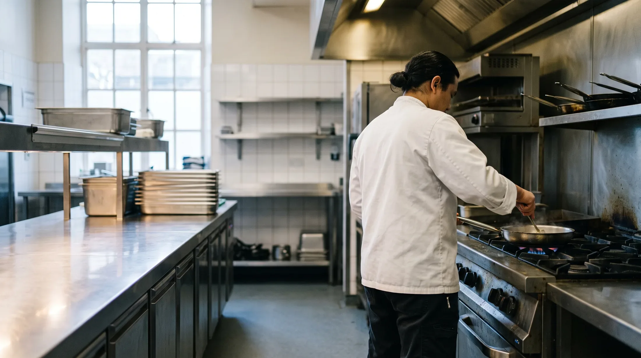 A cook working a pan on the range of a hotel kitchen hot line