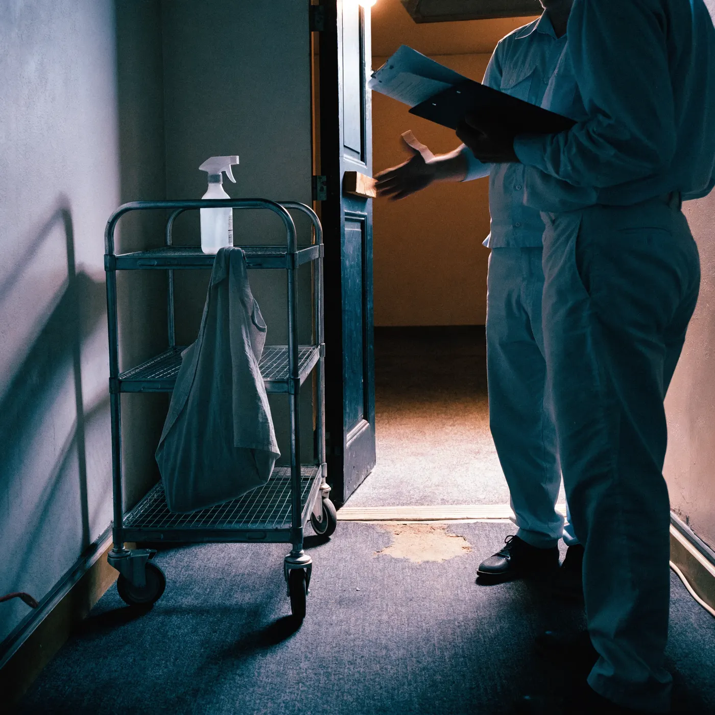 A supervisor with a clipboard talking with a worker beside a cart in a service corridor