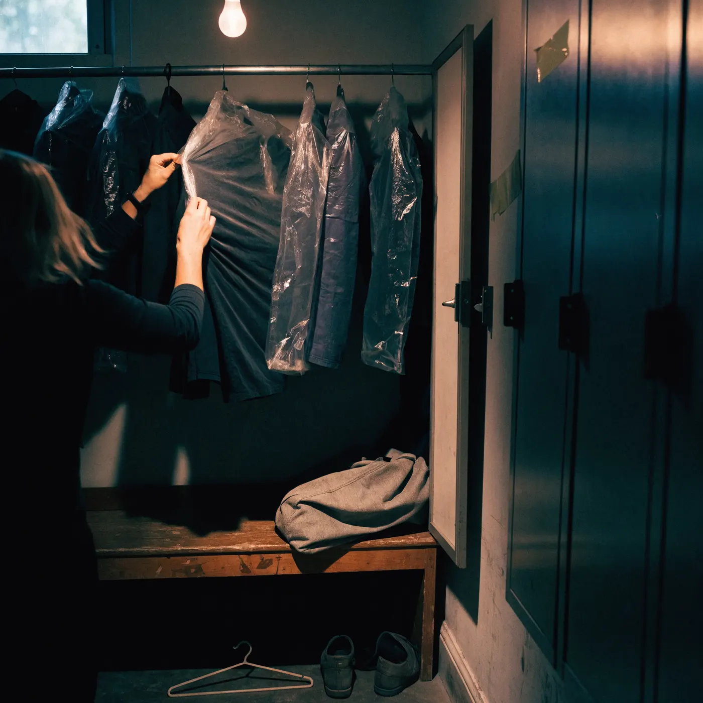 A uniform being lifted from a rail of covered garments in a staff locker room